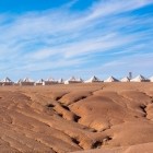 Campo tendato nel deserto di Agafay, tra colline morbide e paesaggi aridi, sotto un cielo ampio e luminoso del Marocco.