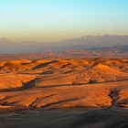 Colline dorate del deserto di Agafay illuminate dal tramonto, con le montagne dell’Atlante che si stagliano sullo sfondo del Marocco.