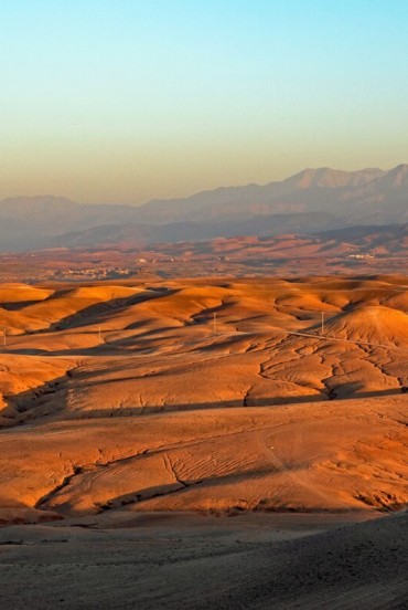 Colline dorate del deserto di Agafay illuminate dal tramonto, con le montagne dell’Atlante che si stagliano sullo sfondo del Marocco.