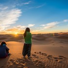 Alba tra le dune di Merzouga, con due viaggiatrici che osservano il sole sorgere sul Sahara, tra silenzi, sabbia dorata e orizzonti infiniti.