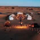 Campo tendato luxury al tramonto a Merzouga tra dune, lanterne e tende eleganti, per vivere il fascino autentico del Sahara marocchino.