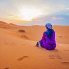 Viaggiatrice seduta sulle dune di Merzouga mentre osserva il sole sorgere sul Sahara, tra silenzi, sabbia dorata e panorami infiniti del deserto.