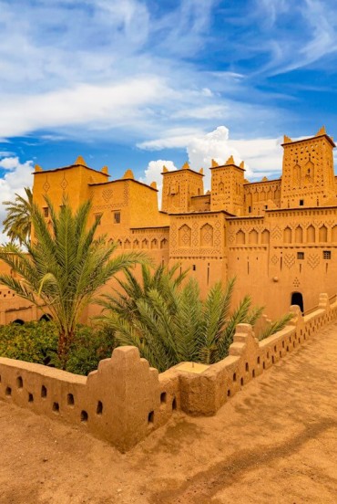 Veduta di una kasbah tradizionale a Ouarzazate, tra mura color ocra, cortili interni, palme e dettagli dell’architettura berbera marocchina.