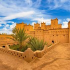 Veduta di una kasbah tradizionale a Ouarzazate, tra mura color ocra, cortili interni, palme e dettagli dell’architettura berbera marocchina.