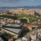 Una spettacolare vista su Atene mette in risalto il Nuovo Museo dell'Acropoli e la collina sacra con il Partenone, dove storia millenaria e città moderna si incontrano.