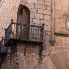 Un balcone in ferro battuto sporge dalla facciata in pietra del centro storico di Cáceres, accanto a uno stemma nobiliare che racconta il passato aristocratico della città medievale.