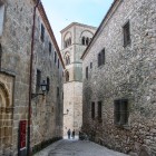 Una stretta via lastricata del centro storico di Trujillo costeggia palazzi nobiliari in pietra e portali scolpiti, guidando lo sguardo verso la torre romanica di Santa María la Mayor.