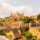 Il ponte di Alcántara attraversa il Tago ai piedi di Toledo, dominata dall’Alcázar e dalle mura medievali che raccontano secoli di storia della Città delle Tre Culture spagnola.