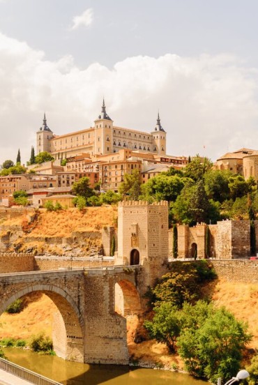 Il ponte di Alcántara attraversa il Tago ai piedi di Toledo, dominata dall’Alcázar e dalle mura medievali che raccontano secoli di storia della Città delle Tre Culture spagnola.