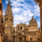 Nel cuore di Toledo, la facciata gotica della Cattedrale Primaziale emerge tra gli edifici storici, scandita da portali scolpiti, guglie e dalla torre del XV secolo.