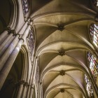 Lo sguardo sale lungo i pilastri gotici della Cattedrale di Toledo fino alle volte a crociera, illuminate da vetrate istoriate che accentuano lo slancio verticale della navata.