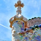 Sulla sommità di Casa Batlló, la torre rivestita di trencadís culmina nella croce a quattro bracci, mentre il tetto squamato evoca il drago di Sant Jordi catalano.