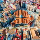 Vista dall’alto, il Mercado de Colón emerge nel cuore dell’Eixample valenciano: la struttura modernista in mattoni dialoga con il fitto reticolo urbano e tetti colorati della città.