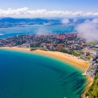 Vista aerea di Santander e della spiaggia di El Sardinero, una lunga distesa dorata lambita dal Mar Cantabrico, tra quartieri costieri, penisole verdi e rilievi.