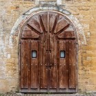 Il portale di San Miguel de Lillo conserva un ingresso raccolto e austero: l’arco in pietra e il massiccio portone ligneo introducono al silenzio del santuario del Naranco.