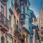 Calle Mon, antica via dei fabbri, sale tra facciate colorate, balconi in ferro e miradores asturiani, guidando lo sguardo verso la torre gotica della Cattedrale di Oviedo.
