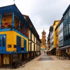 Calle Fierro attraversa il cuore del Fontán tra facciate colorate, balconi fioriti e gallerie vetrate, guidando lo sguardo verso la torre barocca di San Isidoro el Real.