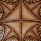 Alzando lo sguardo nel Palazzo Episcopale di Astorga, costoloni in laterizio disegnano una croce geometrica tra motivi traforati: un dettaglio in cui Gaudí fonde tecnica e fantasia.