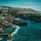 Vista dall’alto, la Piscina Naturale di Isla Cangrejo si apre tra le rocce vulcaniche di Puerto de Santiago, circondata dalle acque turchesi dell’Atlantico e dalle case affacciate sulla costa.