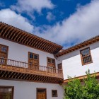 Un elegante cortile coloniale di San Cristóbal de La Laguna è incorniciato da pareti imbiancate, finestre lignee e una lunga balconata canaria, affacciata su un patio raccolto e luminoso.