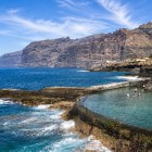 A Puerto de Santiago, una piscina naturale incastonata nella costa vulcanica offre acque limpide, mentre sullo sfondo si stagliano le scogliere di Los Gigantes.