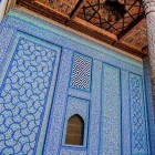 Nel Palazzo Tash-Khauli di Khiva, raffinate maioliche blu e turchesi avvolgono pareti e nicchie, accanto a una preziosa colonna lignea intagliata, espressione dell’arte khanide.