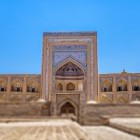 Davanti alla Madrasa Muhammad Rahim Khan II, lo sguardo sale verso il monumentale portale: maioliche blu, archi e mattoni rivelano l’eleganza della Khiva ottocentesca.