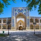 La facciata della Madrasa Nadir Divan-Begi accoglie il viaggiatore con il grande portale, i simurgh e le logge decorate, testimonianza della Bukhara del Seicento.