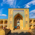La Madrasa Kukeldash, edificata nel XVI secolo, accoglie il viaggiatore con l’alto portale e le logge su due livelli, memoria della Bukhara sulla Via della Seta.Madrasa Kukeldash, construită în secolul al XVI-lea, întâmpină călătorul cu portalul înalt și logiile pe două niveluri, evocând Buhara de pe Drumul Mătăsii.