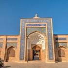 Il grande portale del complesso di Bakhouddin Naqshband, decorato con mosaici e iscrizioni, accoglie pellegrini e visitatori nel cuore spirituale della Bukhara sacra.