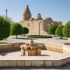 Nel giardino del Mausoleo Chashma Ayub, vasche e alberi conducono lo sguardo verso le cupole, tra cui spicca quella conica ispirata alla tradizione khorezmiana.