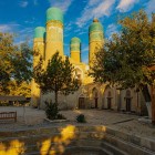 Nel tranquillo cortile della Madrasa Chor Minor, alberi e portici introducono alle quattro torri dalle cupole turchesi, simbolo inconfondibile della Bukhara storica.