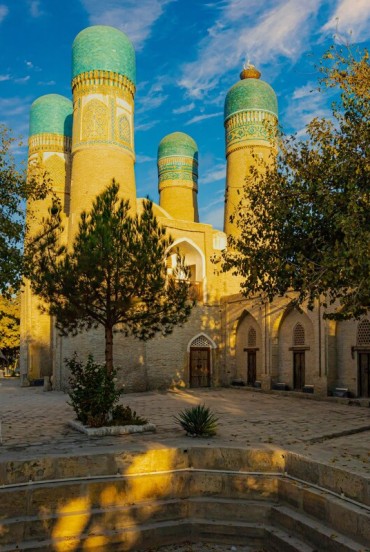 Nel tranquillo cortile della Madrasa Chor Minor, alberi e portici introducono alle quattro torri dalle cupole turchesi, simbolo inconfondibile della Bukhara storica.
