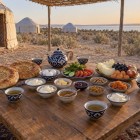 Nel campo di yurte, la colazione uzbeka accoglie il viaggiatore con pane non, tè, frutta e piatti genuini, serviti all’aperto nella quiete luminosa del deserto.