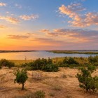 Al tramonto, il Lago Aydarkul riflette le sfumature dorate del cielo, mentre la vegetazione del deserto incornicia un paesaggio silenzioso e sorprendente dell’Uzbekistan.