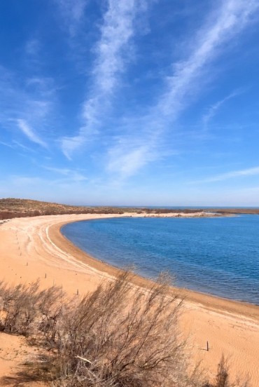 Nel deserto del Kyzylkum, il Lago Aydarkul incontra una lunga spiaggia dorata: acque celesti e dune punteggiate di arbusti creano un sorprendente paesaggio naturale.