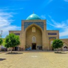 Dai giardini del complesso, il Mausoleo di Kaffal Shashi si mostra da una nuova prospettiva, con il portale monumentale e la cupola che emerge sopra l’edificio.