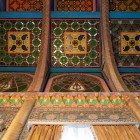 Lo sguardo sale verso un primo soffitto ligneo ornato, composto da vetrate colorate, intagli e motivi geometrici policromi che testimoniano la cura riservata a ogni dettaglio.